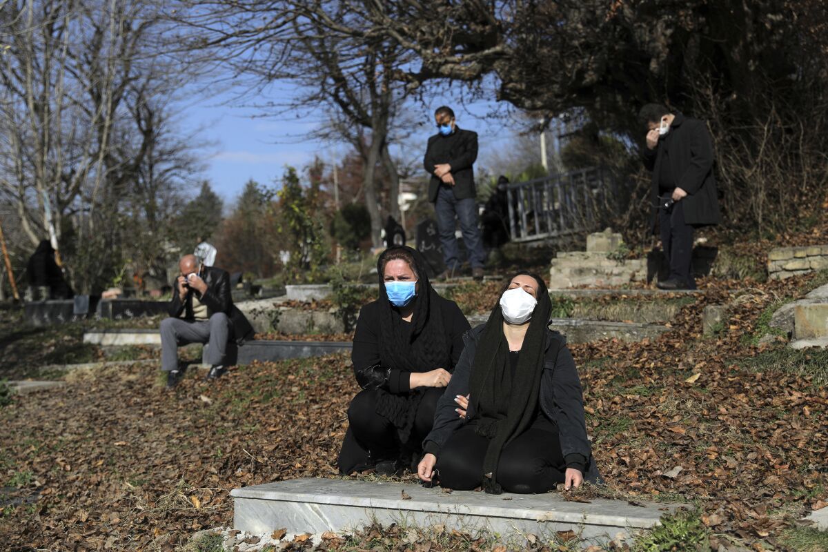 Mourners at a cemetery are socially distanced and masked at an outdoor funeral.