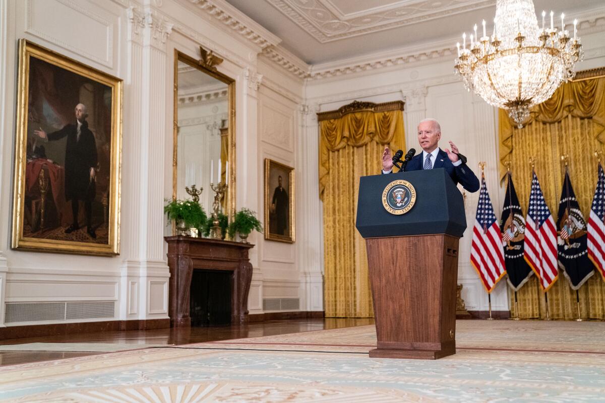 Joe Biden gestures at a lectern with the presidential seal. A portrait of George Washington hangs nearby.