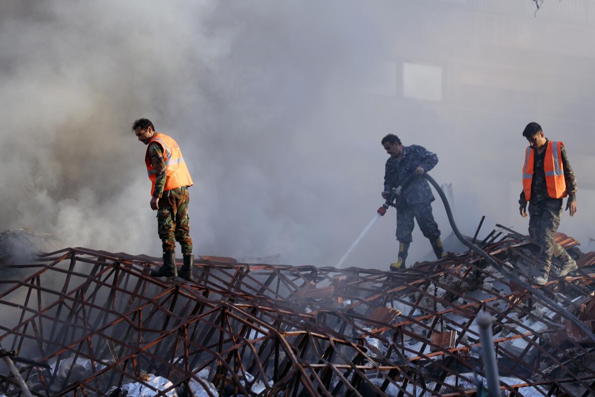 Firefighters douse smoldering ruins.