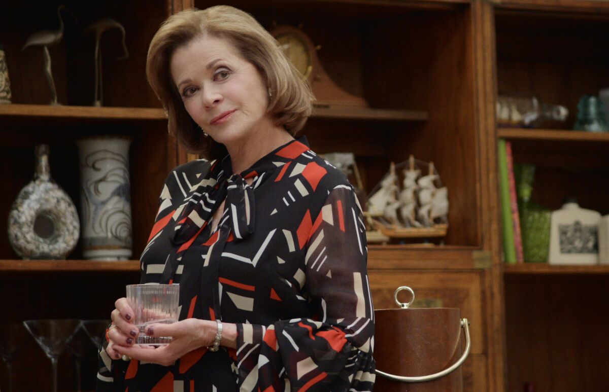 Jessica Walter stands, holding a glass.