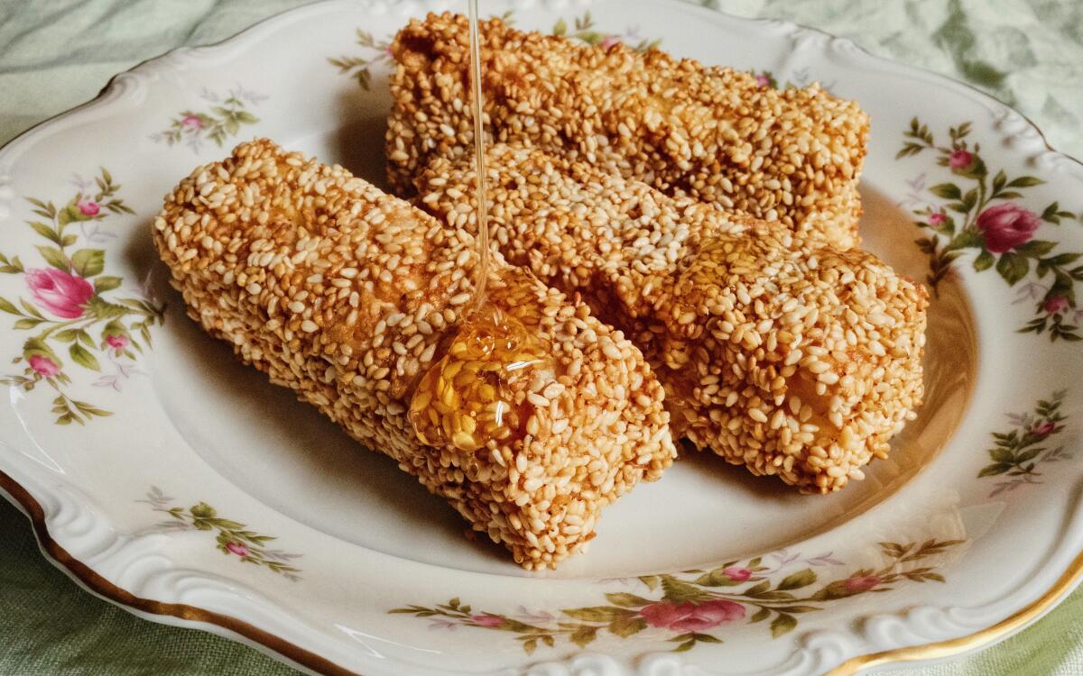 Three sesame-crusted feta sticks drizzled with honey on a flower-patterned china plate.