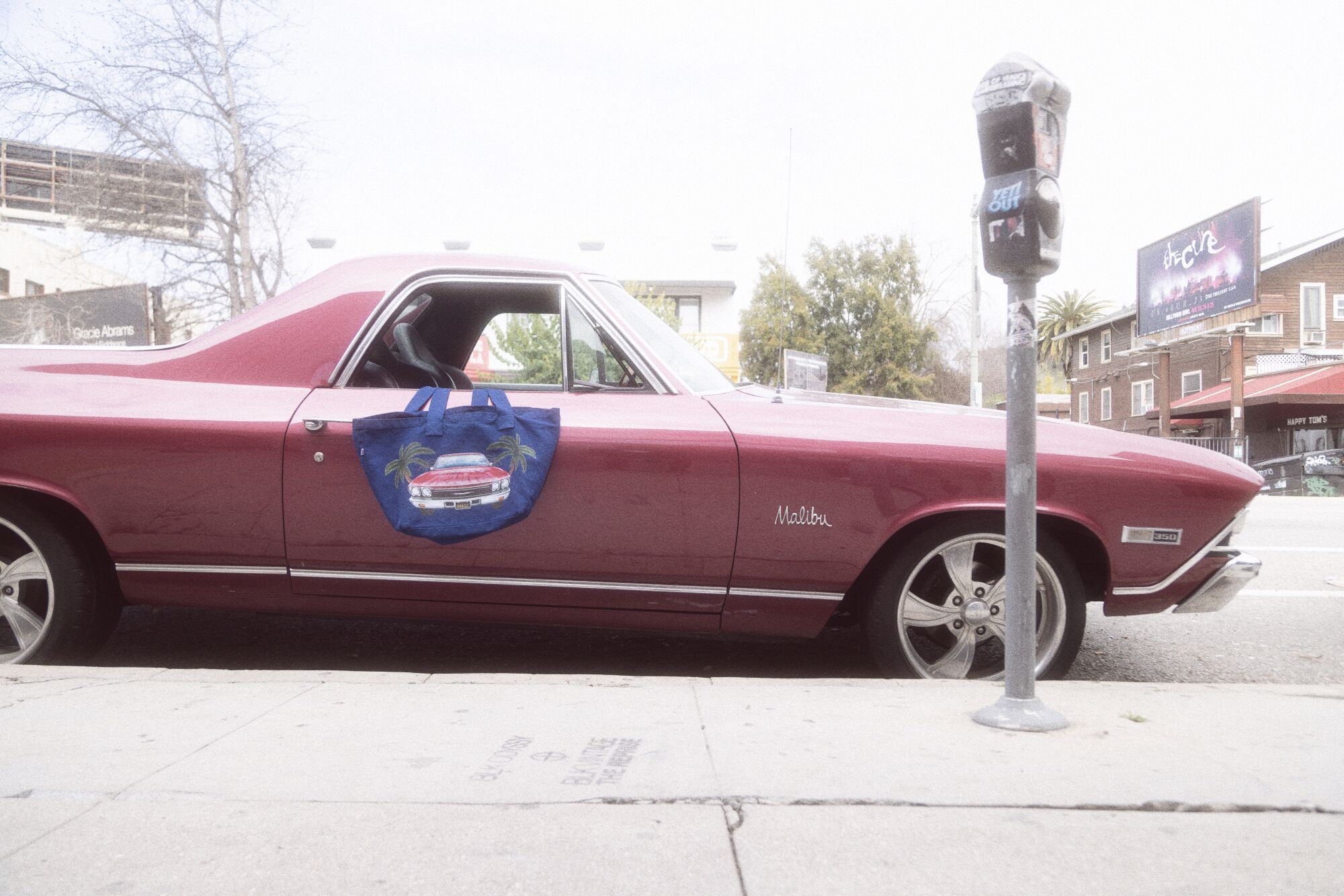 A parked pink El Camino with a blue tote bag hanging out of the window.