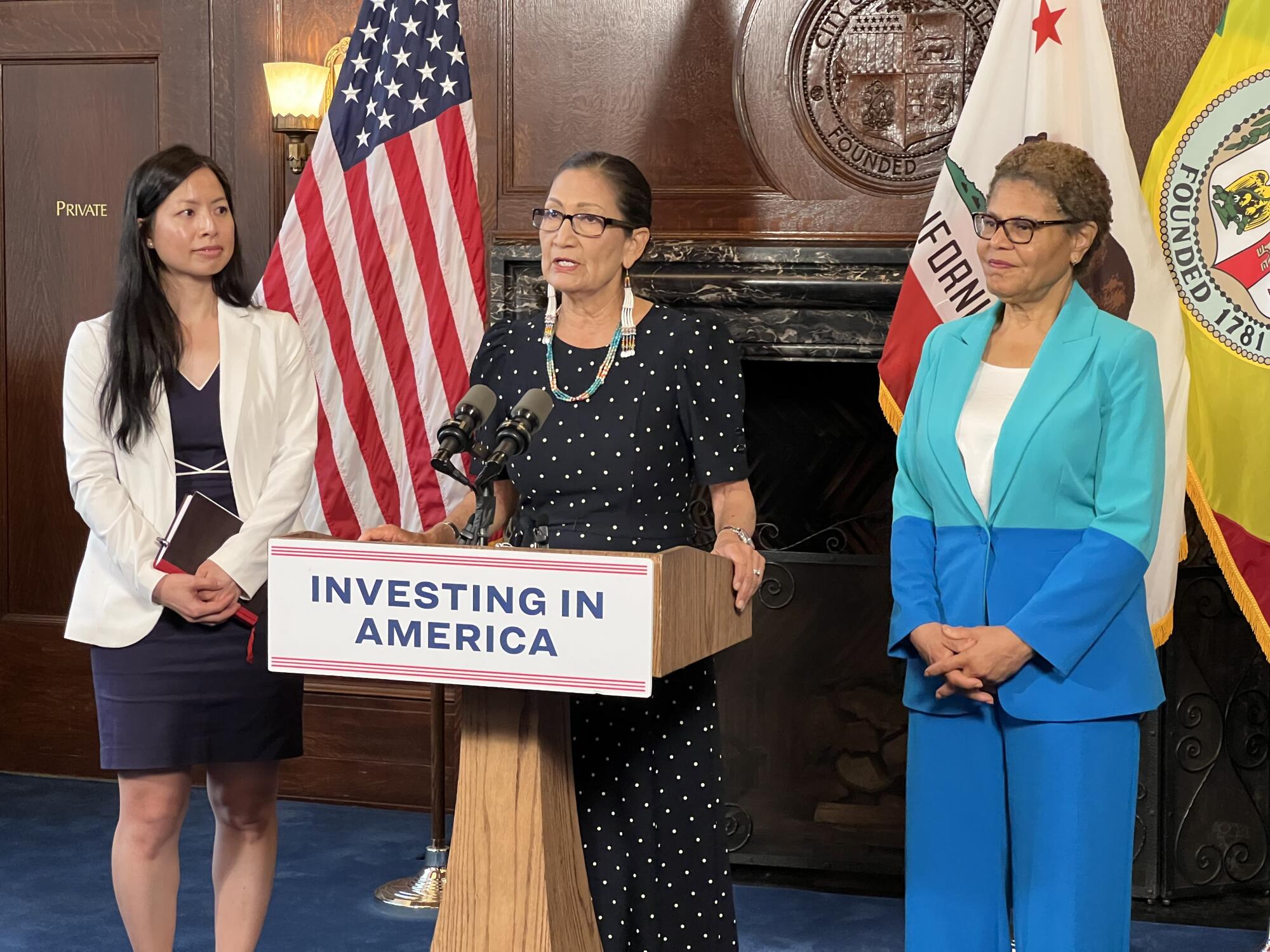 U.S. Secretary of the Interior Deb Haaland speaks at a lectern, flanked by officials Le-Quyen Nguyen, left, and Karen Bass.