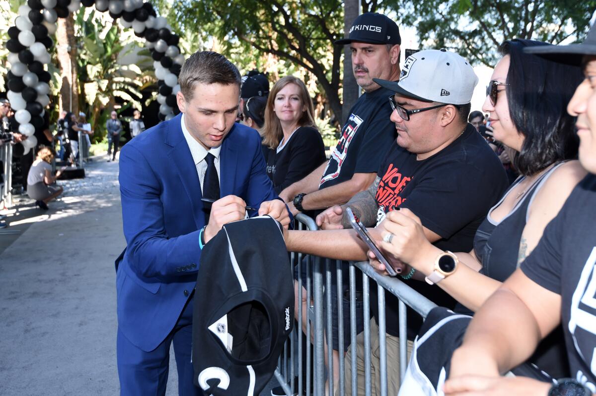 Blake Lizotte, in a blue suit and black tie, autographs a jersey before the Kings' home opener against the Predators on Oct. 12 at Staples Center.