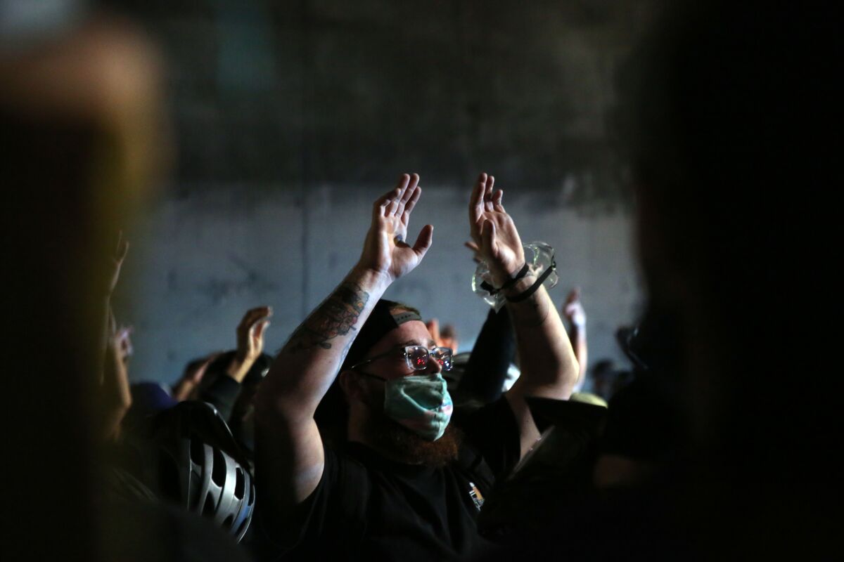 Demonstrators in downtown L.A. hold their hands up as police gather during a protest over the shooting of Jacob Blake.