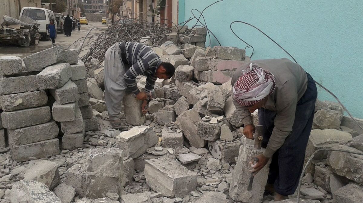 Fouad Salim, left, and Khalef Attiyeh, chip at chunks of concrete recovered from a destroyed home to shape them into blocks. It's the only building material some residents can afford in the west Mosul neighborhood of Jadidah.