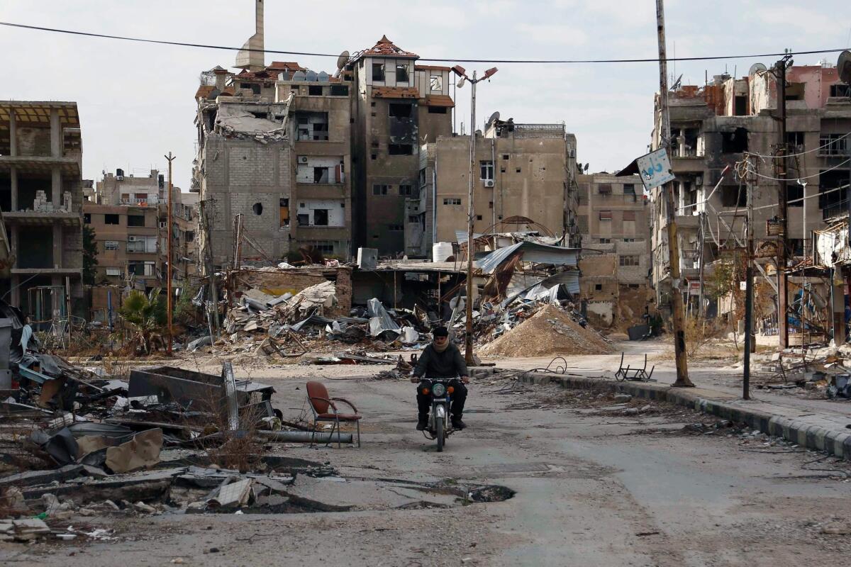 A man drives his motorbike past damaged buildings in Harasta, east of the Syrian capital of Damascus, on Feb. 10.