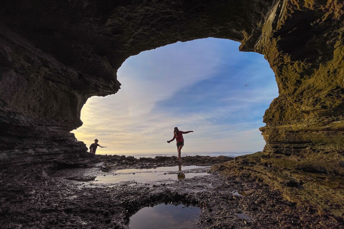 A person silhouetted against a partly cloudy blue sky in the opening of a sea cave.