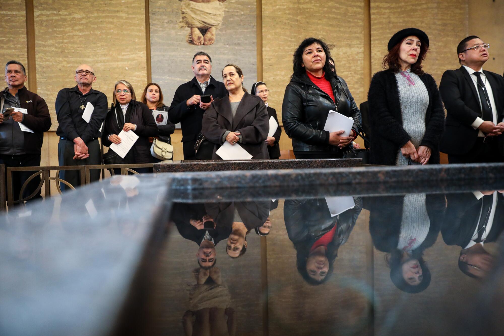 Visitors are reflected in the baptismal font as they wait 