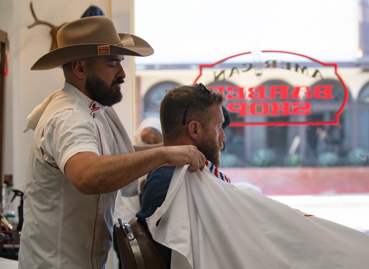 AJ Trujillo fits an apron onto a client at American Barbershop in Orange on Thursday.