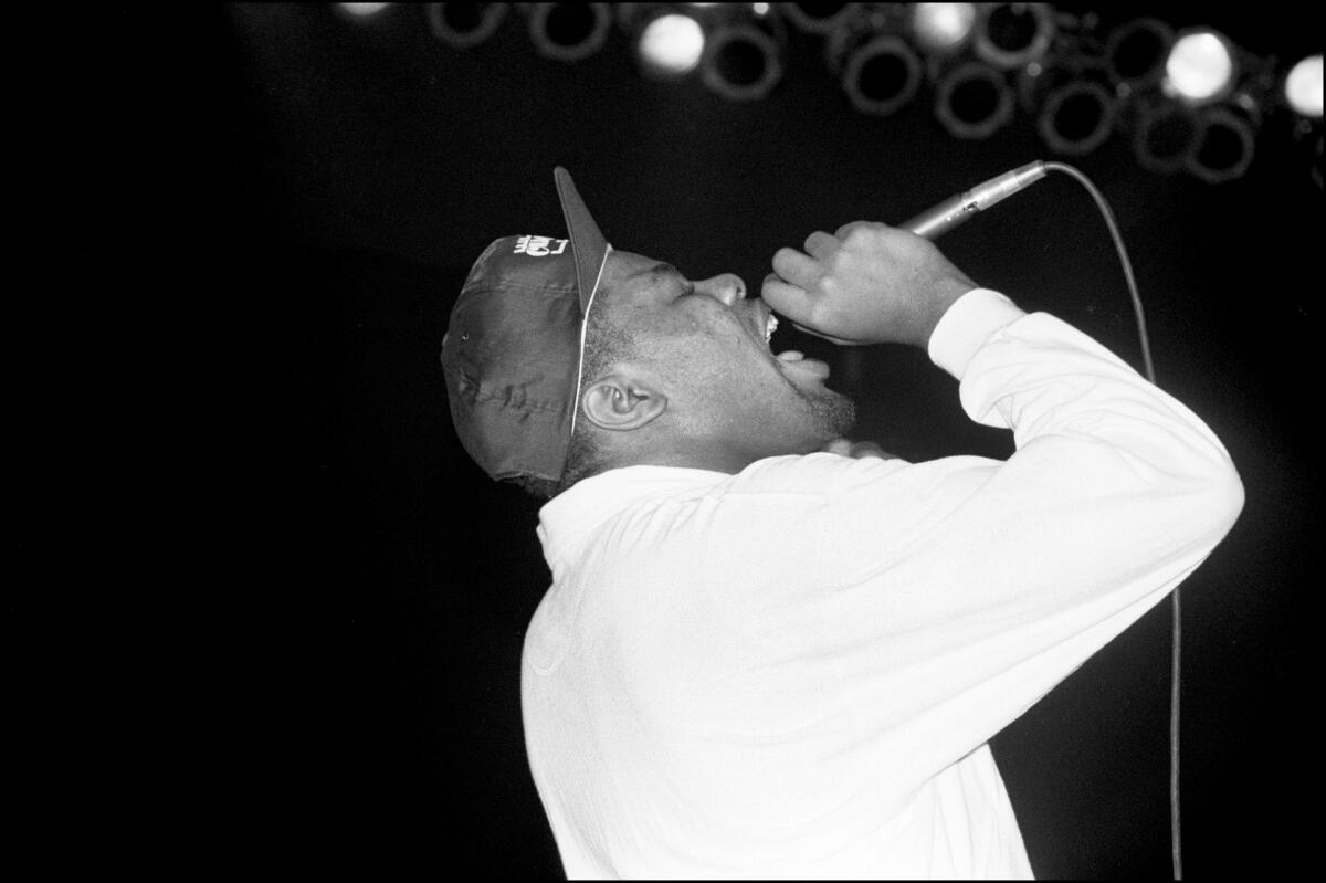 Biz Markie, in a cap with upturned brim, leans back as he raps into a microphone.