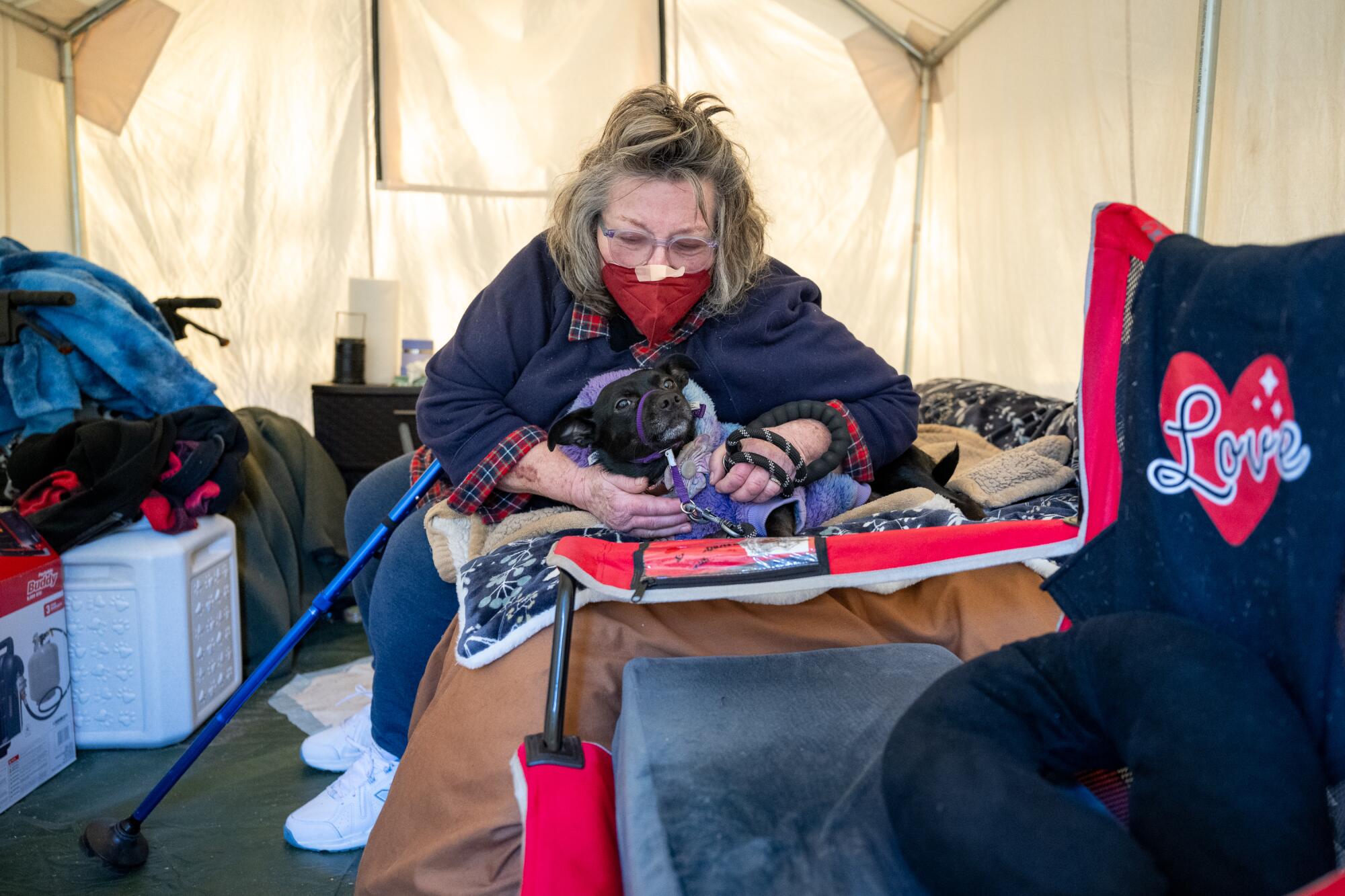 A woman plays with her dog in a tent at a homeless encampment.