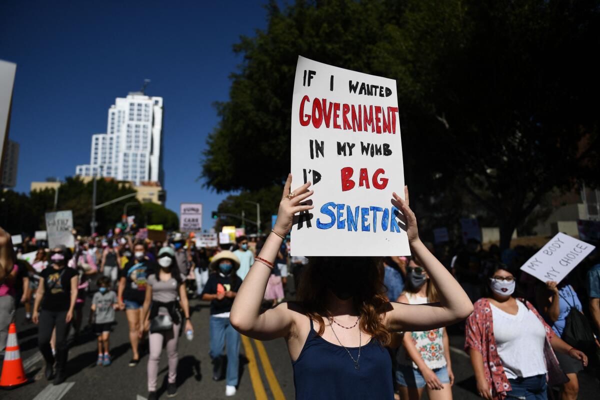  Women's March participants hold signs while walking down a street