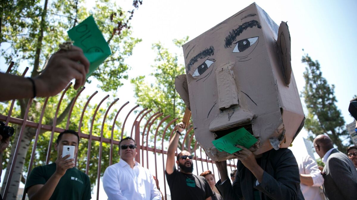 Members of the East Yard Communities for Environmental Justice demonstrate against Gov. Jerry Brown on Wednesday. Cindy Donis, wearing the Brown mask, pretended to consume oil company money.