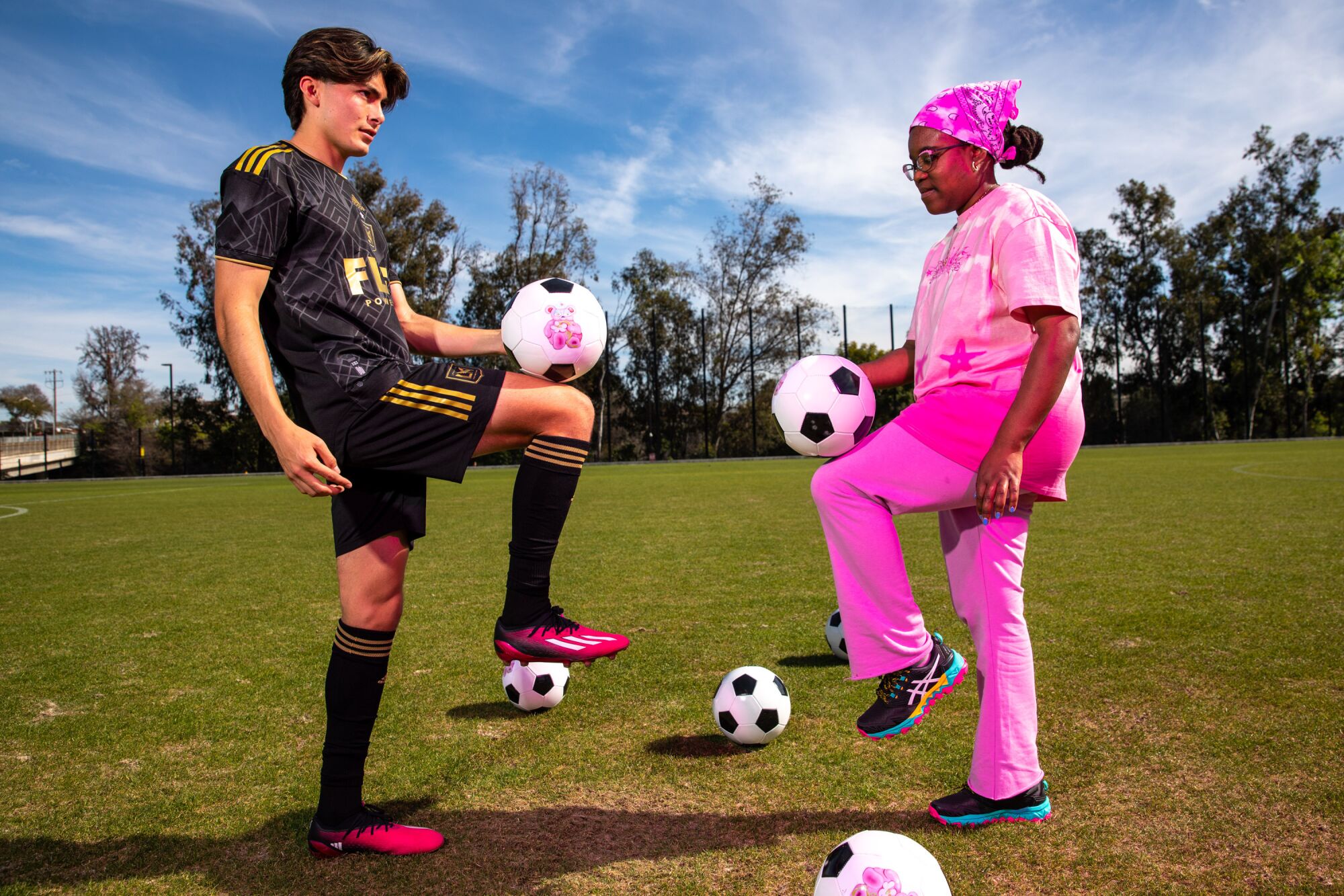 A man in a black shirt and shorts and a woman in a pink outfit with soccer balls on a field.