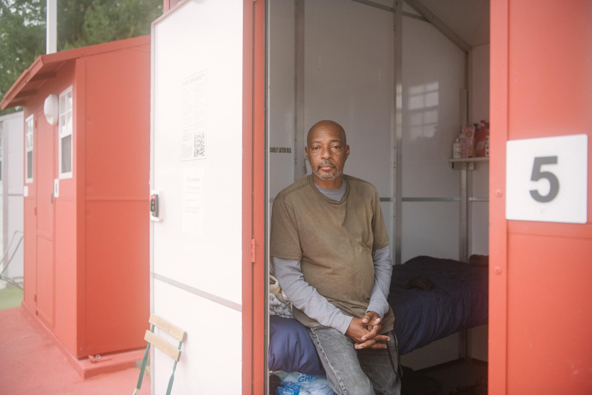 Portrait of a person sitting in the doorframe of a red tiny house