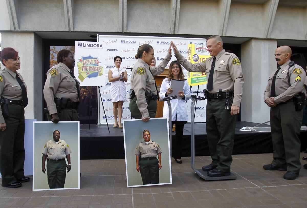 Los Angeles County Sheriff's Deputy Pearl Cruz, center, holding a portrait of herself before she lost 17.2% of her starting weight, congratulates Deputy Sheriff Brian Knott for his weight loss. [For the record: An earlier version of this caption incorrectly identified Deputy Sheriff Brian Knott as Sgt. Todd Knight.]