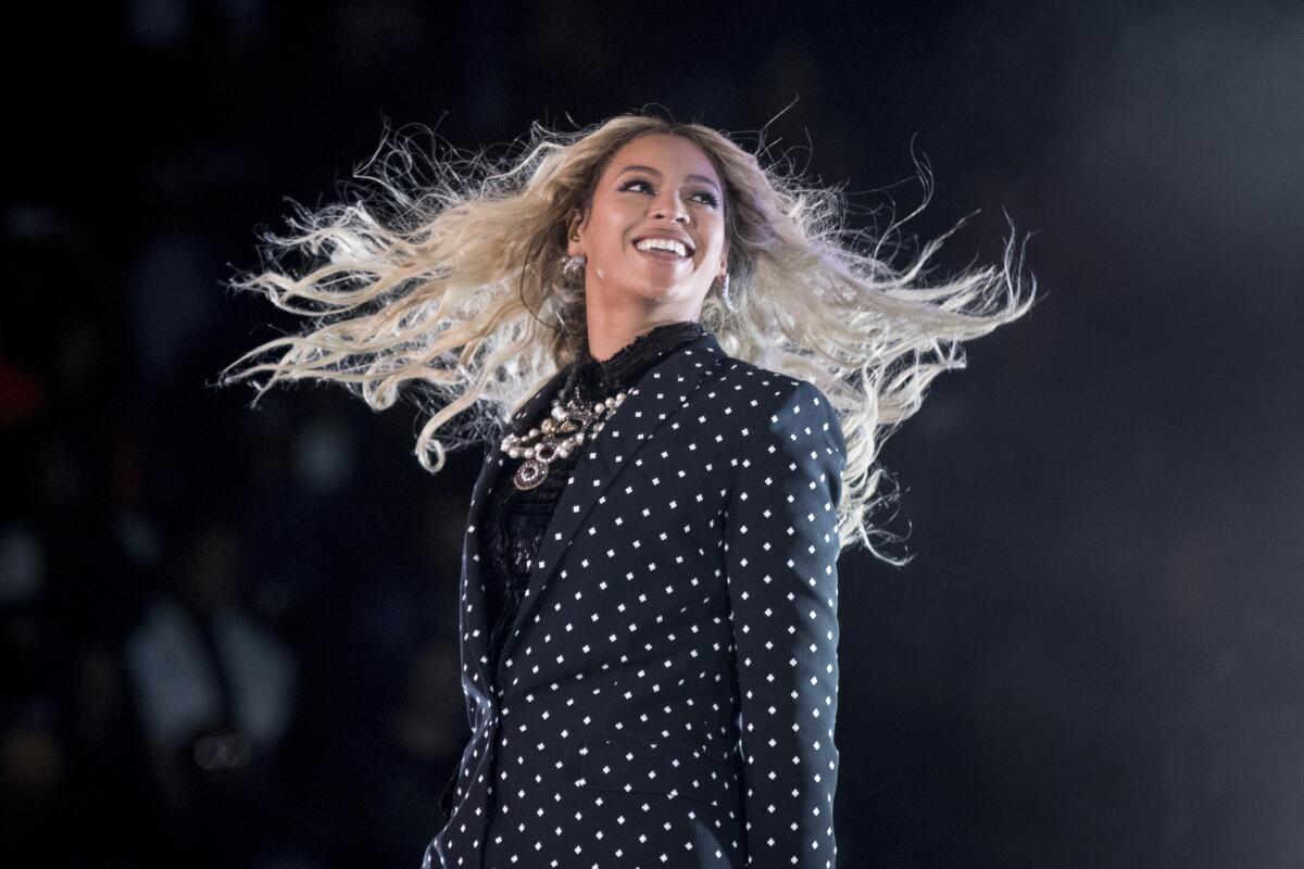 A smiling Beyoncé wears a polka-dot pantsuit as the wind blows  her hair