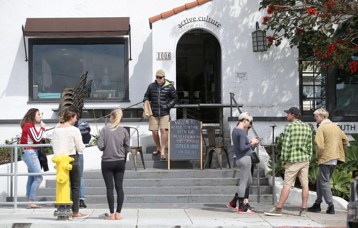 Small groups wait on the sidewalk for phone-in pickup orders at Active Culture in Laguna Beach as businesses work to comply with directives to avoid public gatherings and uphold social distancing guidelines during the coronavirus pandemic.