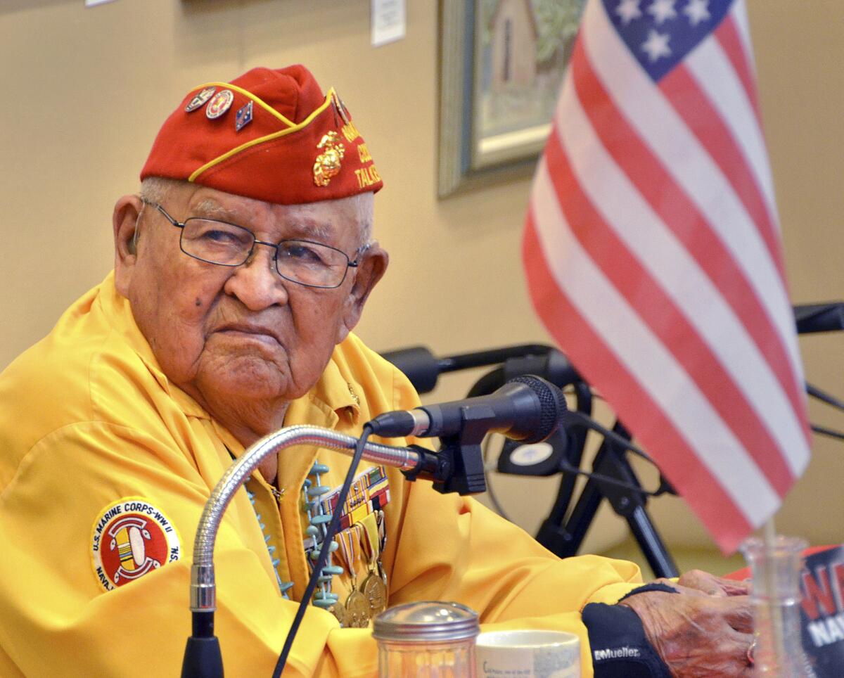 Navajo code talker Samuel Sandoval wears medals and a red cap and yellow jacket. 