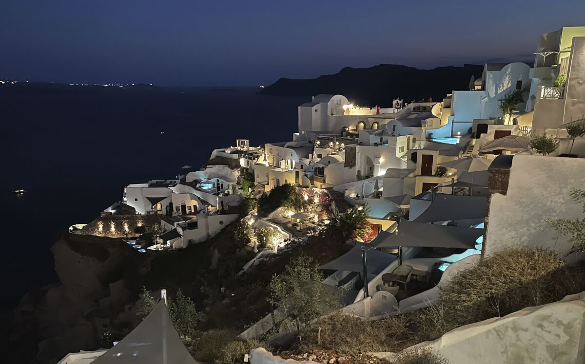 At night, the blue lights of pools and Jacuzzis of luxurious hotels illuminate a village on the island of Santorini, Greece.