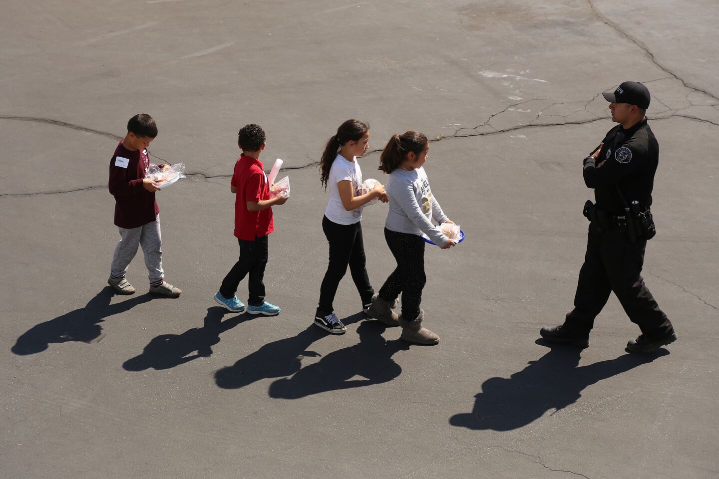 A police officer leads children to be reunited with their parents at Cajon High School after a school shooting at North Park Elementary School.