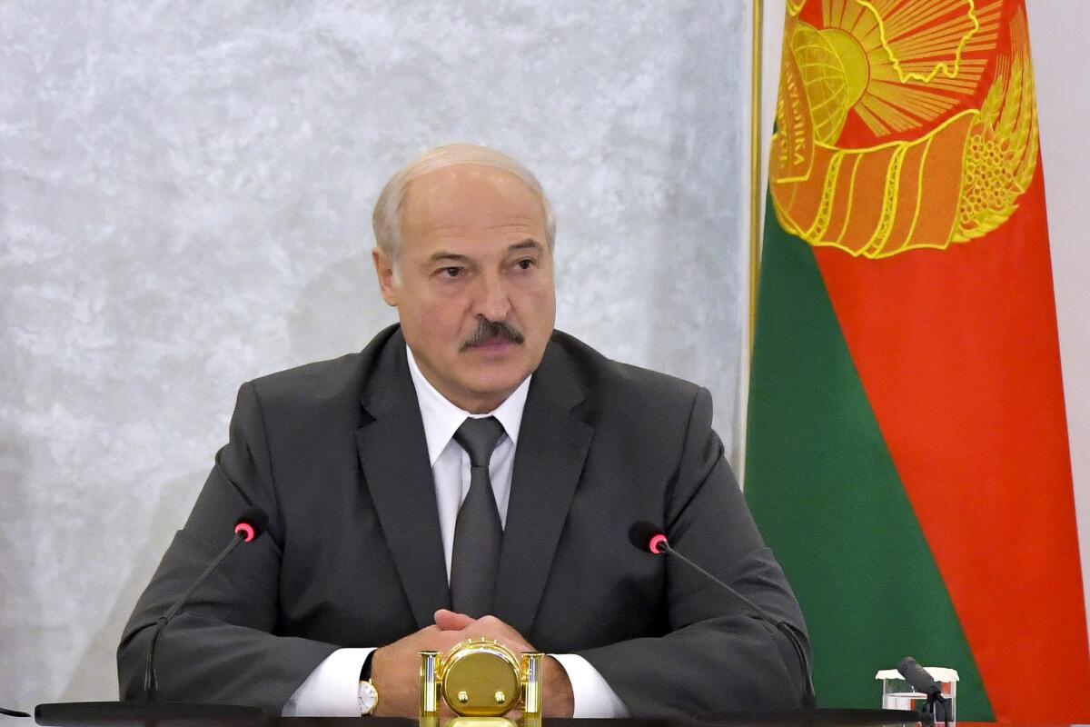 Belarusian President Alexander Lukashenko sits with hands folded in front of a flag.