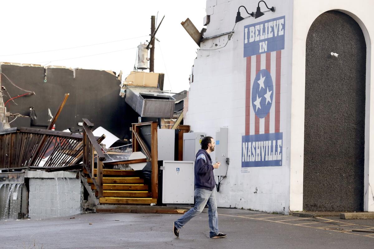 In this March 3, 2020, file photo, a man walks by The Basement East, a live music venue, on March 3, 2020, after a tornado hit Nashville, Tenn. It has been nearly a year since deadly storms tore across Nashville and other parts of Tennessee, killing more than 20 people and damaging more than 140 buildings. (AP Photo/Mark Humphrey, File)