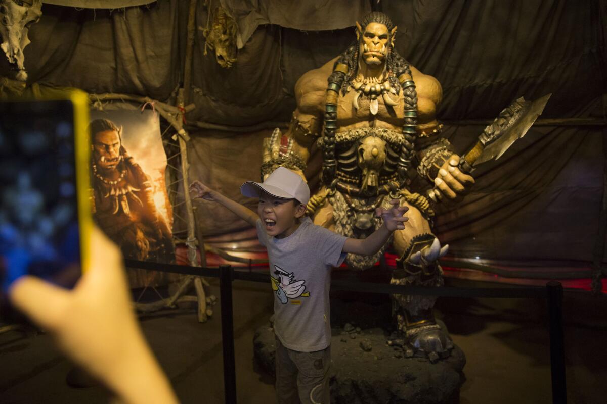 A child poses in front of a statue of a character from the movie "Warcraft" in Beijing on Friday. "Warcraft" has a strong fan base in China.
