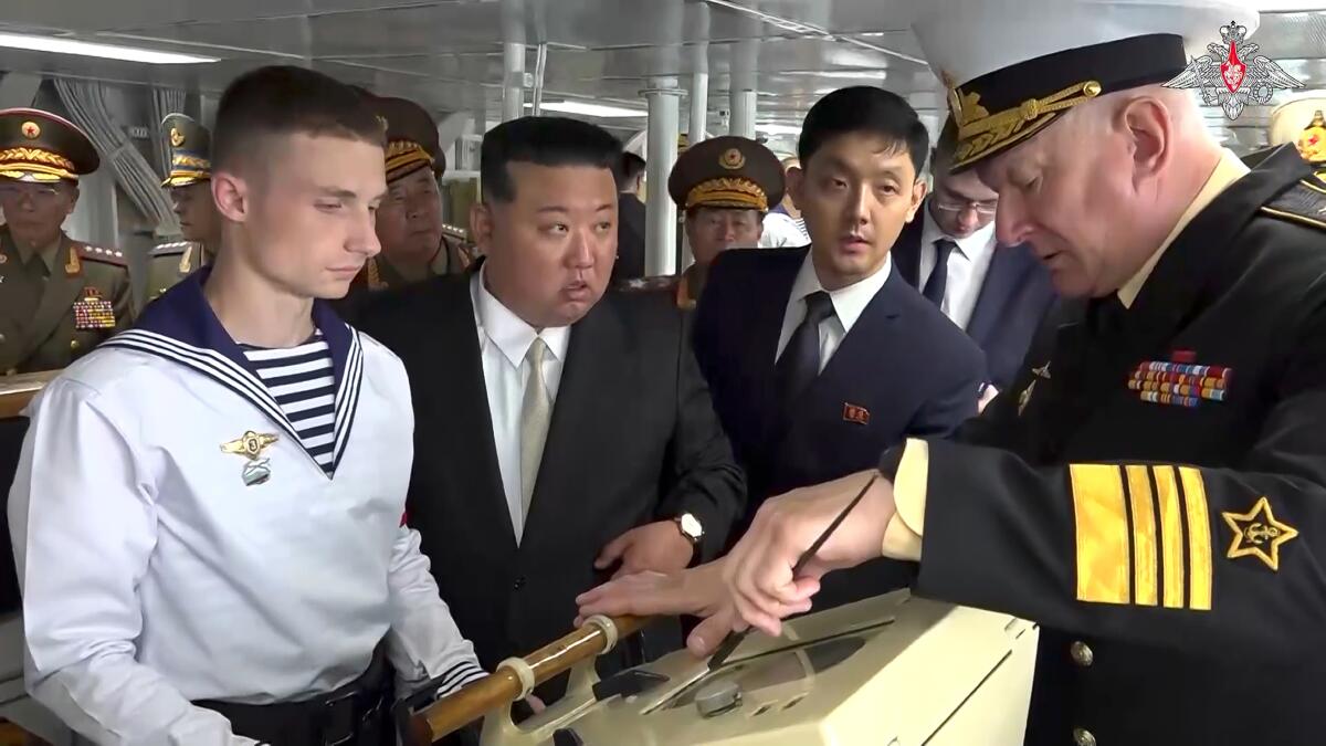 Men, some in naval uniforms, look at a panel on a ship. 