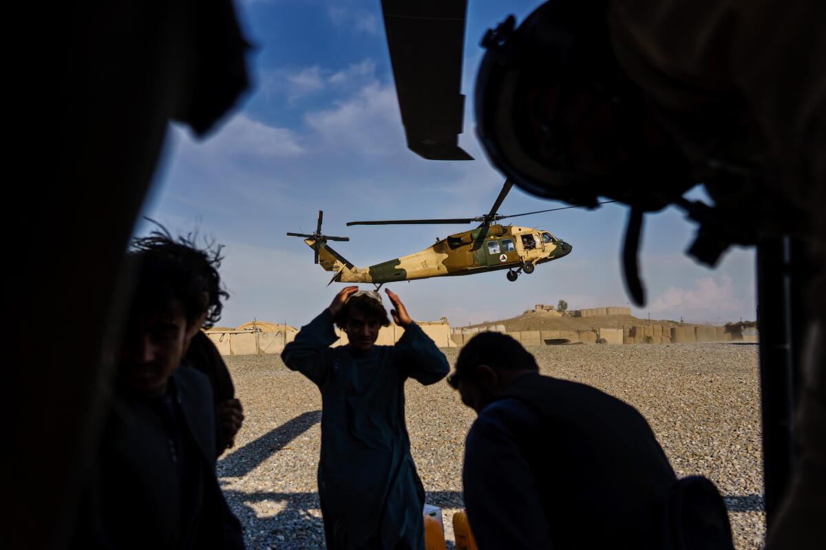  Silhouetted people appear far in front of a descending helicopter.