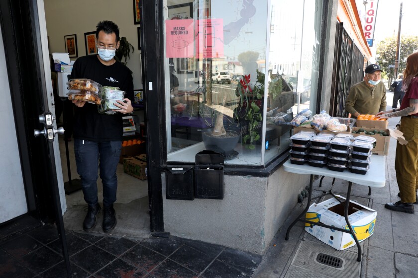A man carries boxes of food through a doorway to a table with more boxes of food 