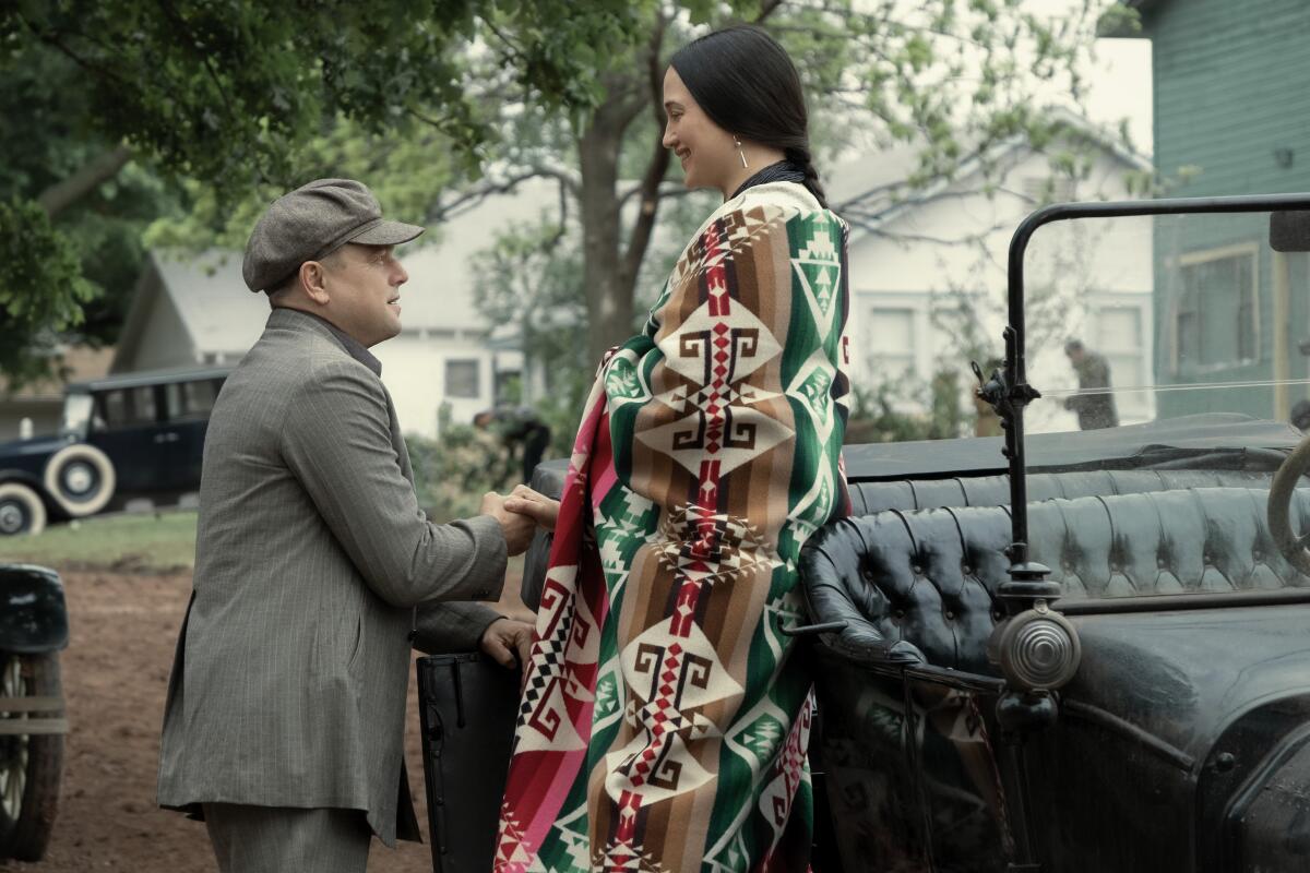 A man takes a woman's hand and guides her out of a car.