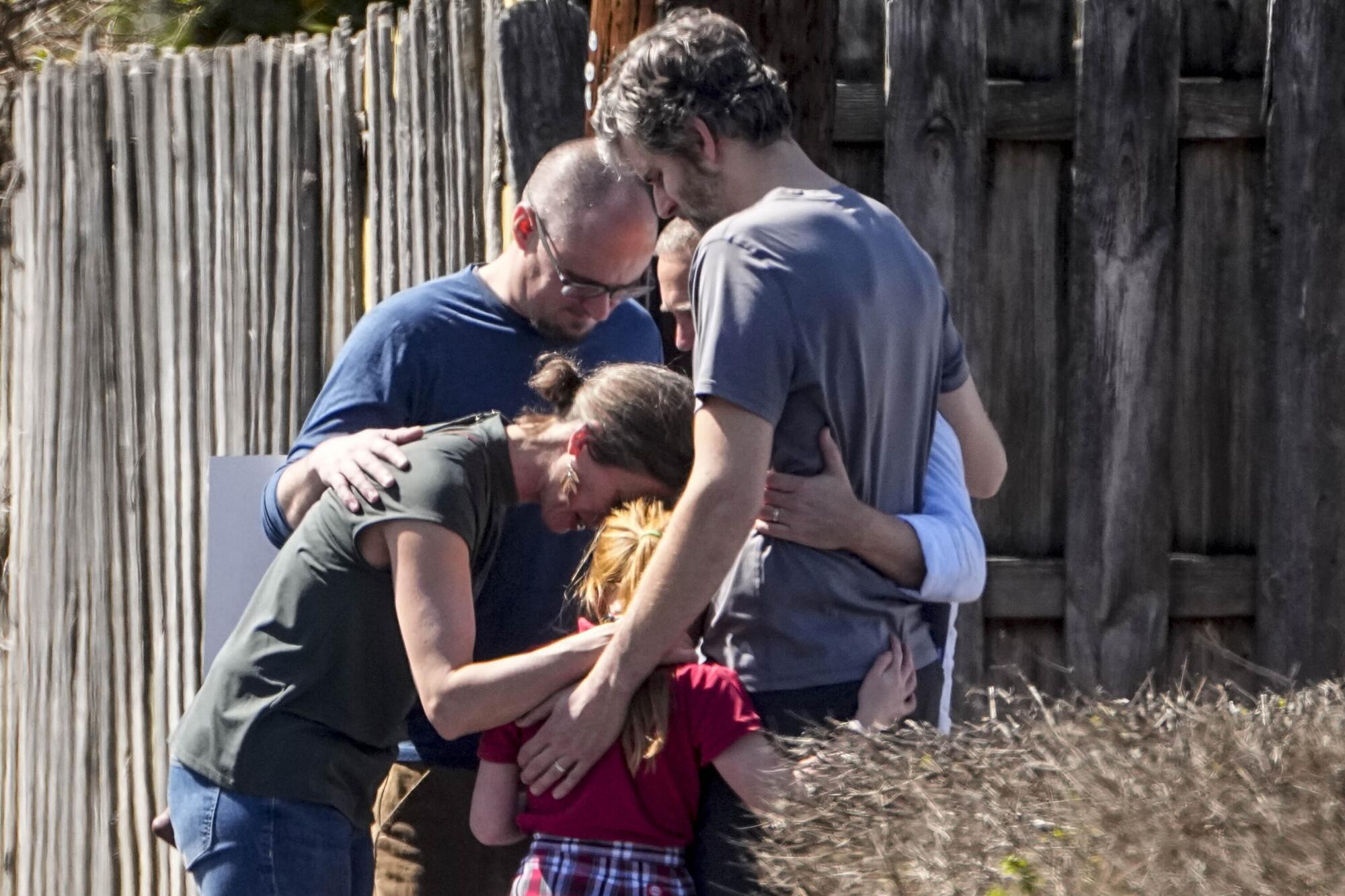 A small group of people embrace with bowed heads.