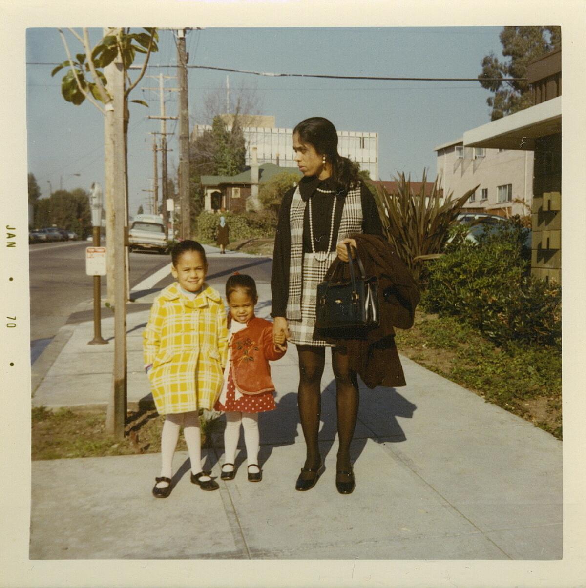 Two girls and their mother standing on a sidewalk. 