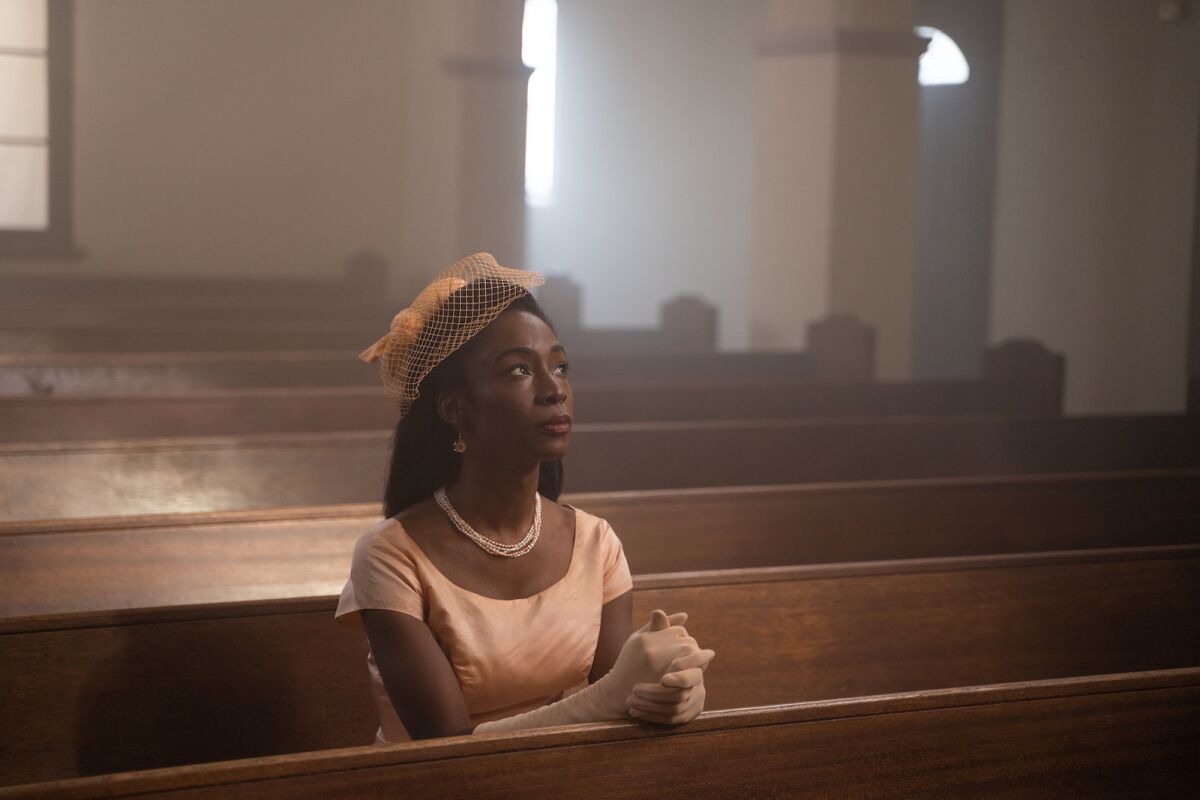 A woman seated with hands clasped in prayer in a pew of a church in the movie "Framing Agnes."