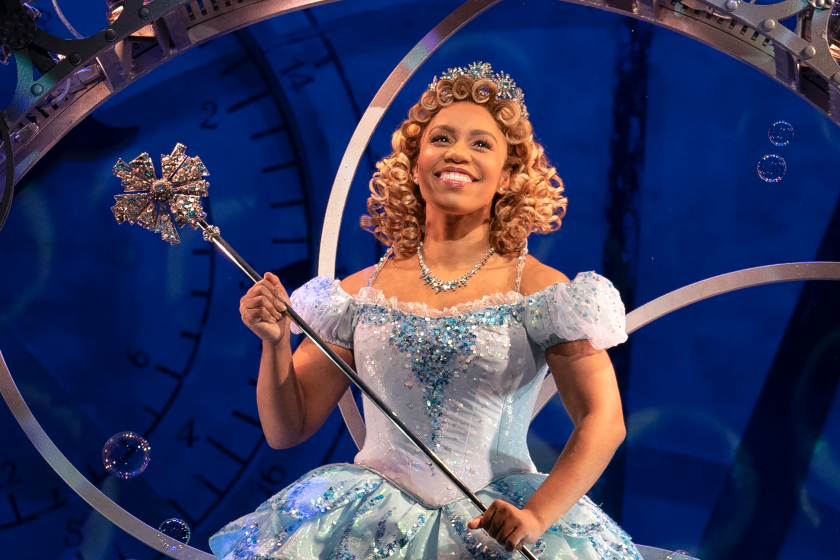 A woman with curly blond hair wearing a blue ball gown and wielding a magic scepter