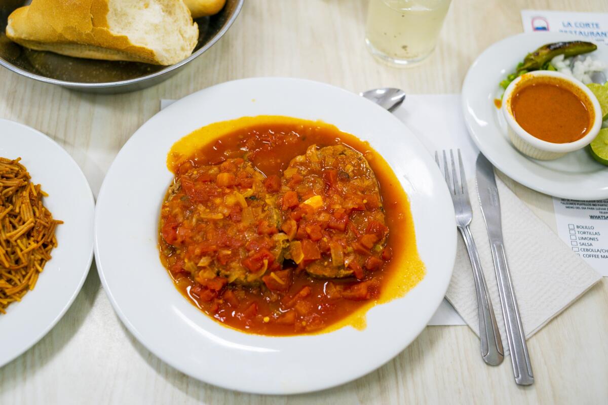 A red-hued dish next to plates holding sauce and bread.