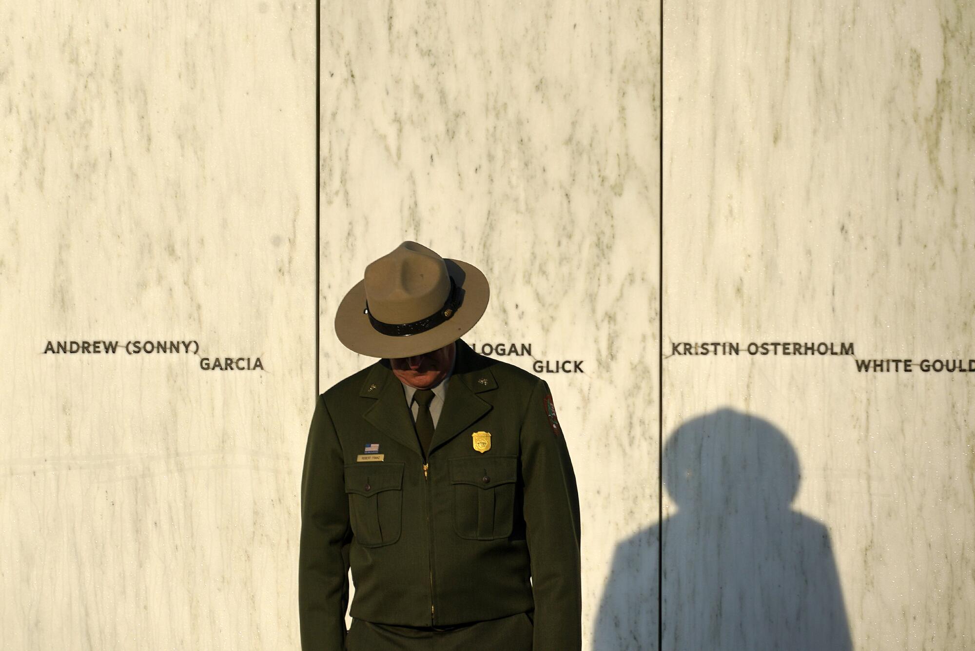 A National Park Service ranger stands in front of the Wall of Names with head bowed.