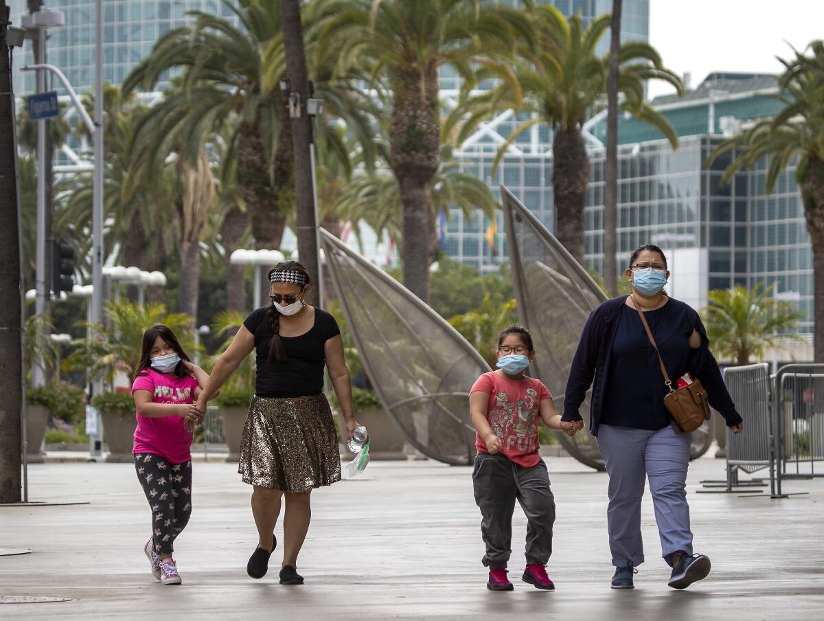 Two women and two children walk while wearing masks.