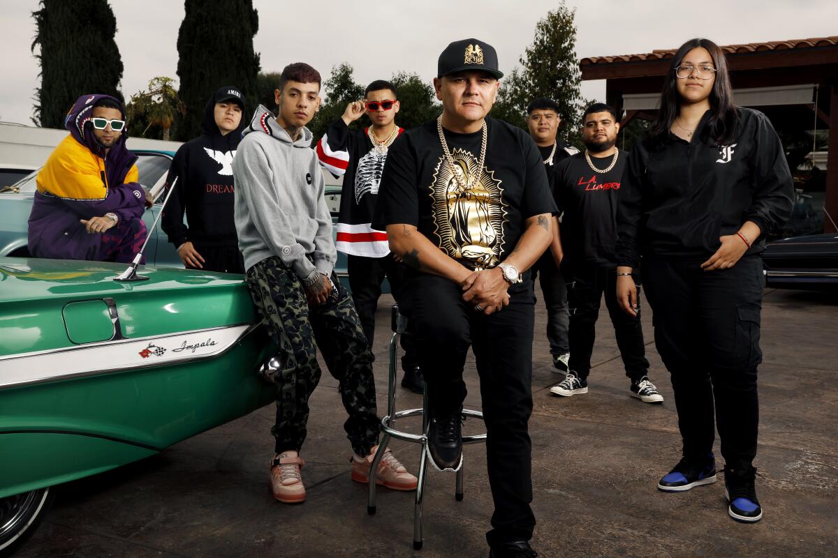 Jimmy Humilde poses with artists signed to his record label Rancho Humilde next to a vintage Chevrolet Impala.