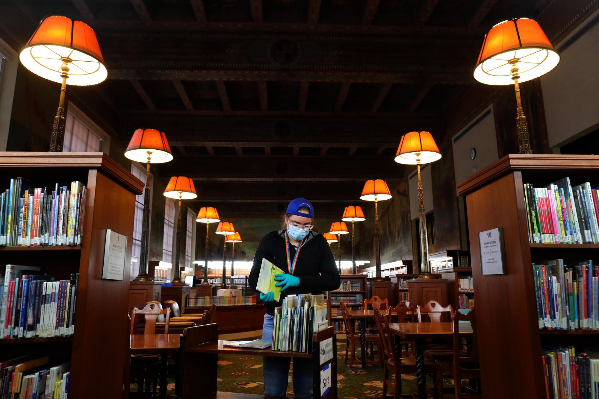 A woman leans over a cart of books.