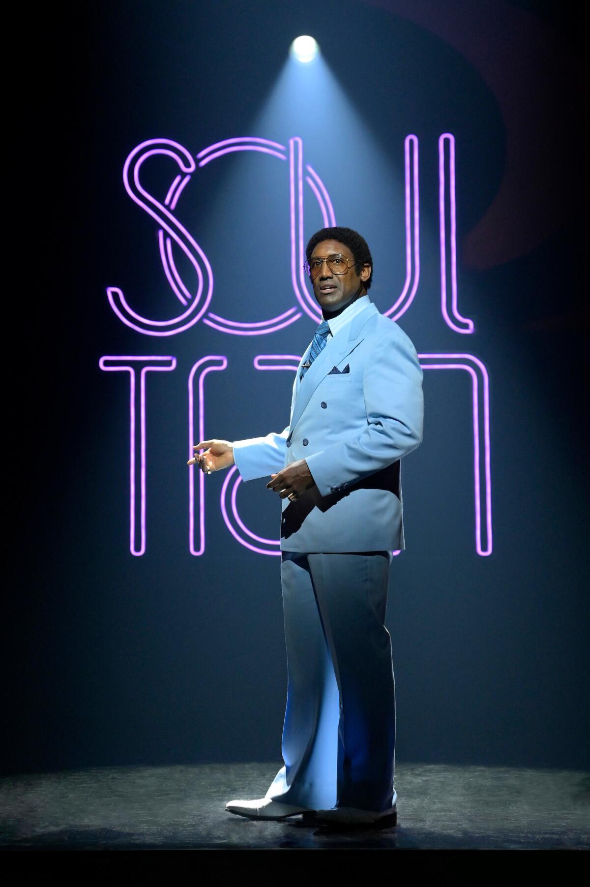 A man in a powder blue suit stands in front of a neon sign that says Soul Train