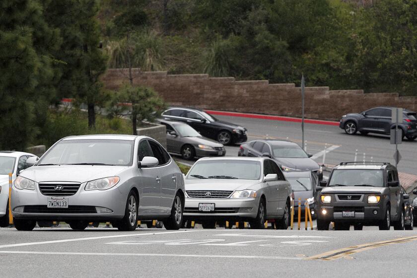 A line of vehicles backed up onto Mountain Street for the GCC food bank at Glendale Community College on Tuesday, April 7, 2020. With GCC shut down due to coronavirus, the campus food pantry converted today to a mobile food pantry not only for students but for anybody. Motorists backed up onto the Mountain Street to turn onto College Driveway to be lead through the open-air parking lot into the parking structure where campus staff loaded vehicles with the donated food.