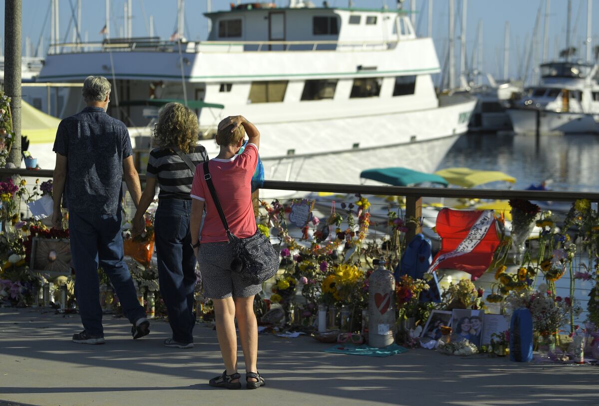 FILE - In this Sept. 6, 2019 file photo people visit a growing memorial to the victims who died aboard the dive boat Conception as its sister boat Vision sits in the background, in Santa Barbara, Calif. The owner of the scuba diving boat company has announced an indefinite suspension of its fleet in the wake of the fatal boat fire off the Southern California coast that killed 34 people. Truth Aquatics Inc. says Tuesday, Oct. 1, 2019 on its Facebook page that the company will "dedicate our entire efforts to make our boats models of new regulations" in collaboration with the Coast Guard and the National Transportation Safety Board. (AP Photo/Mark J. Terrill,File)