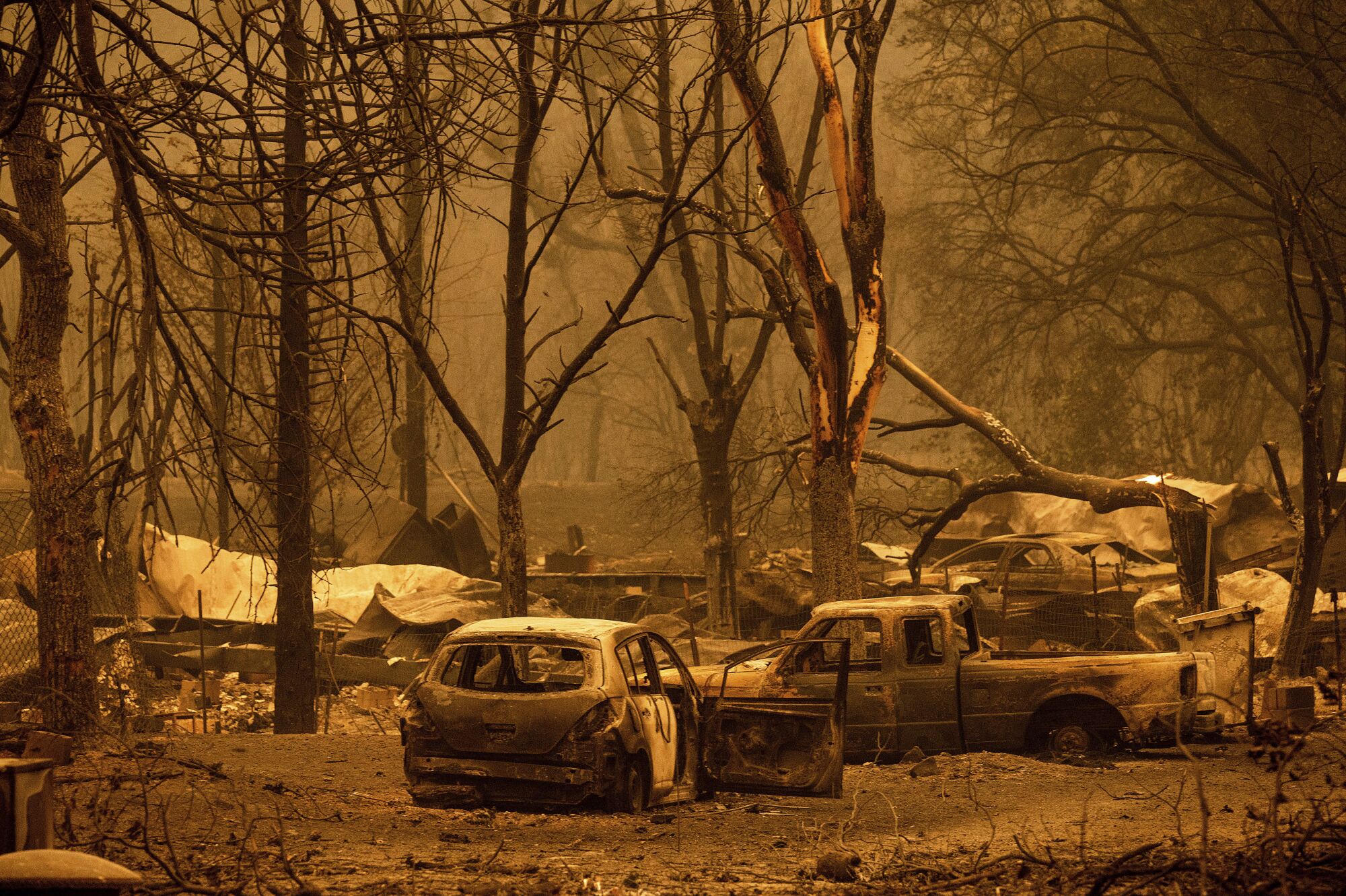 Burned homes, cars and trees in a smoky landscape.