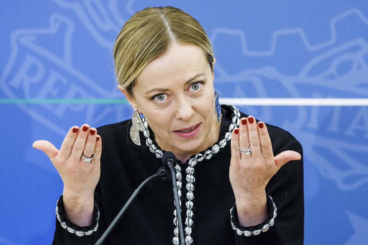 Italy's Premier Giorgia Meloni, wearing a dark suit, gestures with her hands as she talks to the media.