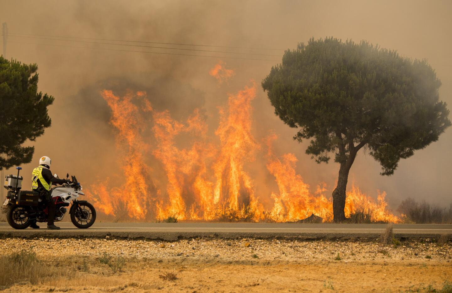 A military police officer stands by his motorcycle next to flames from a forest fire near Mazagon in southern Spain on June 25, 2017.