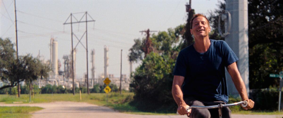 A man rides a bicycle near an industrial building.