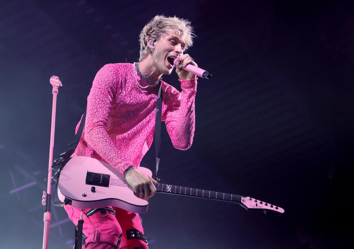 A male singer, in pink shirt and pants, holds a pink guitar and sings into a pink microphone.